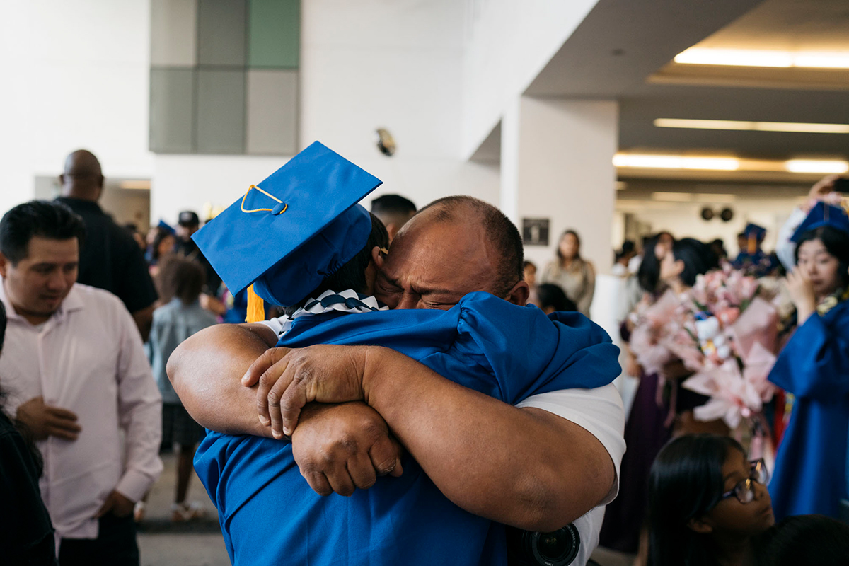 A father tightly hugs his child, a high school student wearing a blue graduation cap and gown