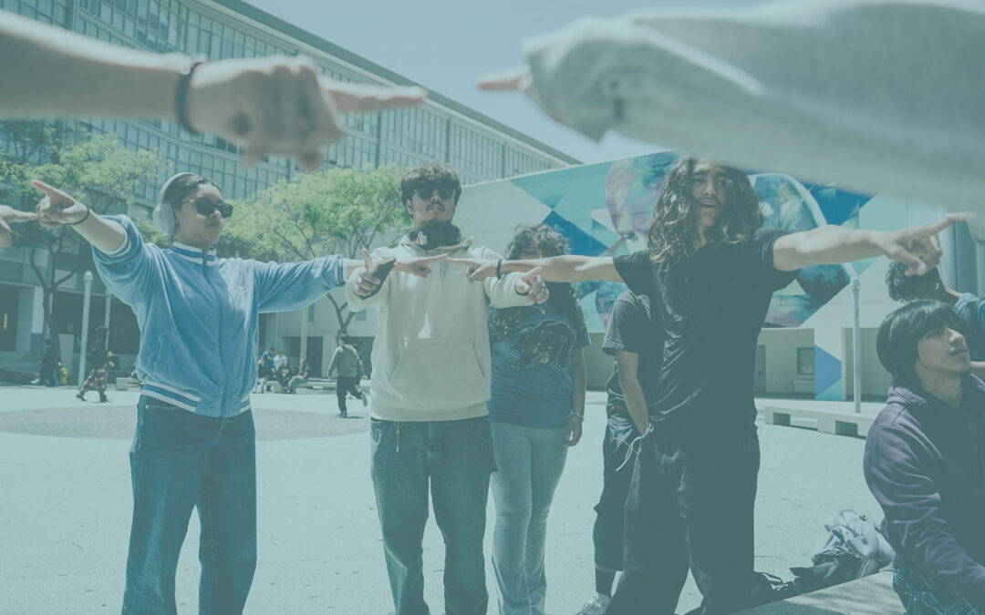A group of teenagers on a school campus stand in a circle with the arms outstretched towards each other