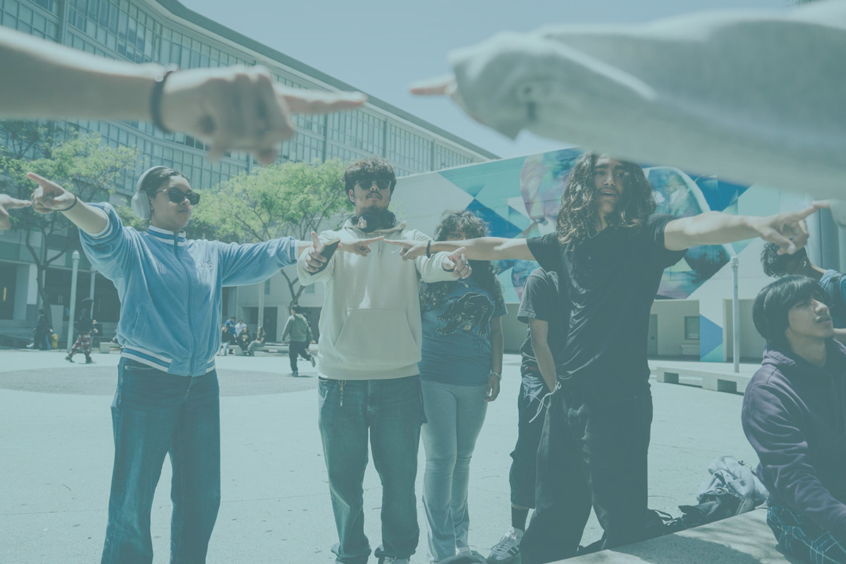 A group of teenagers on a school campus stand in a circle with the arms outstretched towards each other